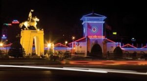 Chợ Bến Thành về đêm với cổng đồng hồ chiếu sáng, tượng cưỡi ngựa phía trước và dải sáng giao thông