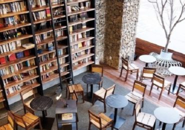 Quán cafe sách với kệ sách cao, bàn tròn và ghế gỗ trong không gian yên tĩnh