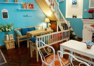 Không gian quán cafe nhỏ ấm cúng tông xanh với ghế sắt trắng và bàn gỗ