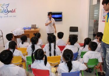 Trẻ em mặc áo blouse trắng ngồi trên ghế nhiều màu nghe hướng dẫn viên