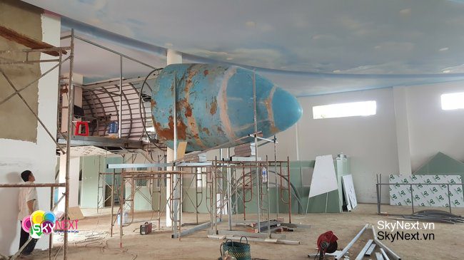 Mô hình cấu trúc hình bầu dục màu xanh đang treo giữa giàn giáo xây dựng